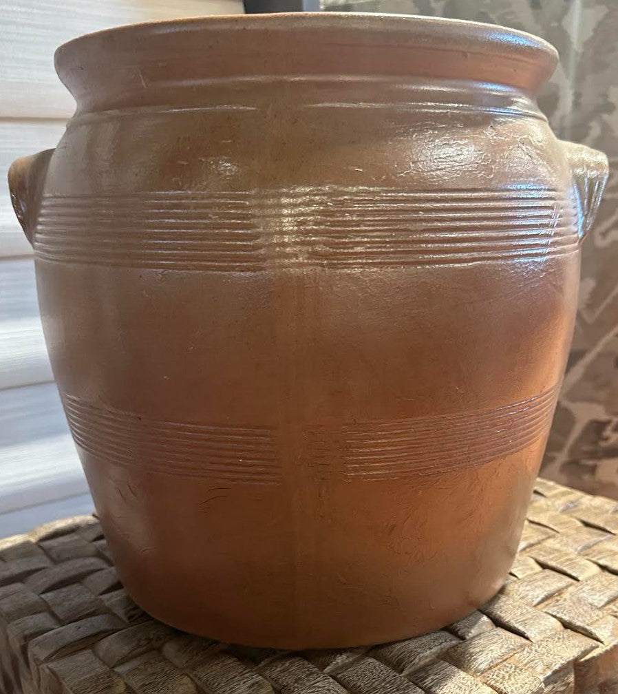 Brown ceramic jar with textured surface on a woven surface