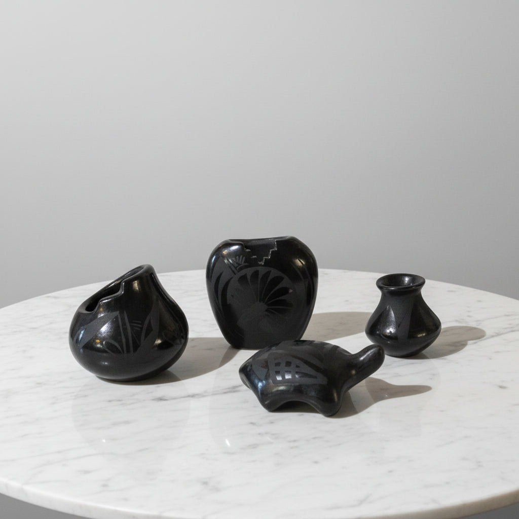 A collection of black Santa Clara miniature pottery pieces on a white surface, with one piece facing the camera and the others in different orientations.